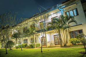 Ein mehrstöckiges Hotel mit einem Balkon im zweiten Stock, umgeben von gepflegten Rasenflächen und unterschiedlichen Pflanzen.