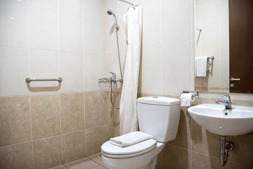 A bathroom with a toilet, a shower with a curtain, a sink, and a towel rack.
