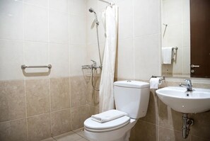 A bathroom with a toilet, a shower with a curtain, a sink, and a towel rack. - RUKUN Resort Sentul (Kab. Bogor)