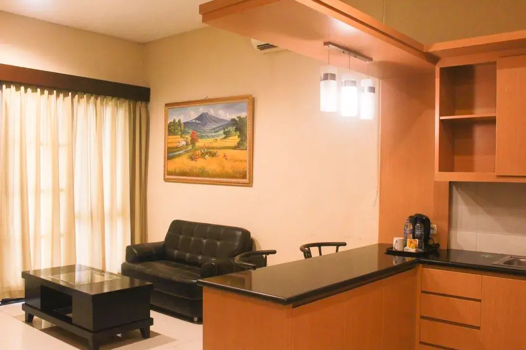 A compact living space with a sofa, a small coffee table, a kitchen area with a countertop, and a painting on the wall.