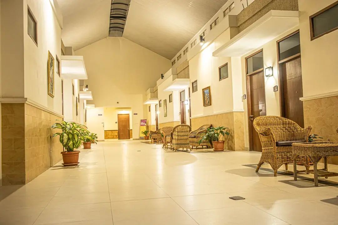 Een hotellobby met een lange gang, rieten meubels, potplanten en een trap aan het einde.