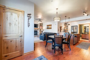 A spacious living area with a wooden floor, a dining table with chairs, a kitchen with wooden cabinets, and a fireplace. - Trailhead Lodges 711 | Walk Downtown, Hot Tub (Winter Park)