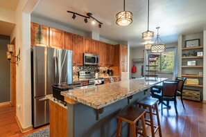 A modern kitchen with stainless steel appliances, wooden cabinets, a large island with bar stools, and pendant lighting. - Trailhead Lodges 711 | Walk Downtown, Hot Tub (Winter Park)