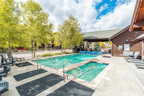 Ein Schwimmbecken mit Holzterrasse, Liegestühlen und einer überdachten Liegefläche.