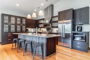 A modern kitchen with dark wood cabinets, a large island with bar stools, stainless steel appliances, and pendant lighting. - Tabernash Retreat | 3BR, Hot Tub, Mtn Views (Tabernash)