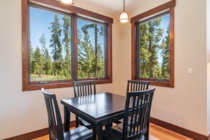 A dining area with a table and chairs, large windows with a forest view, and a pendant light. - Tabernash Retreat | 3BR, Hot Tub, Mtn Views (Tabernash)