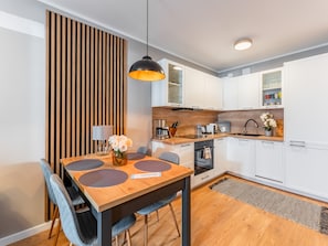 A modern kitchen with white cabinets, a wooden countertop, and a dining area with a wooden table and chairs. - Apartament Kołłątaja (Kołobrzeg)