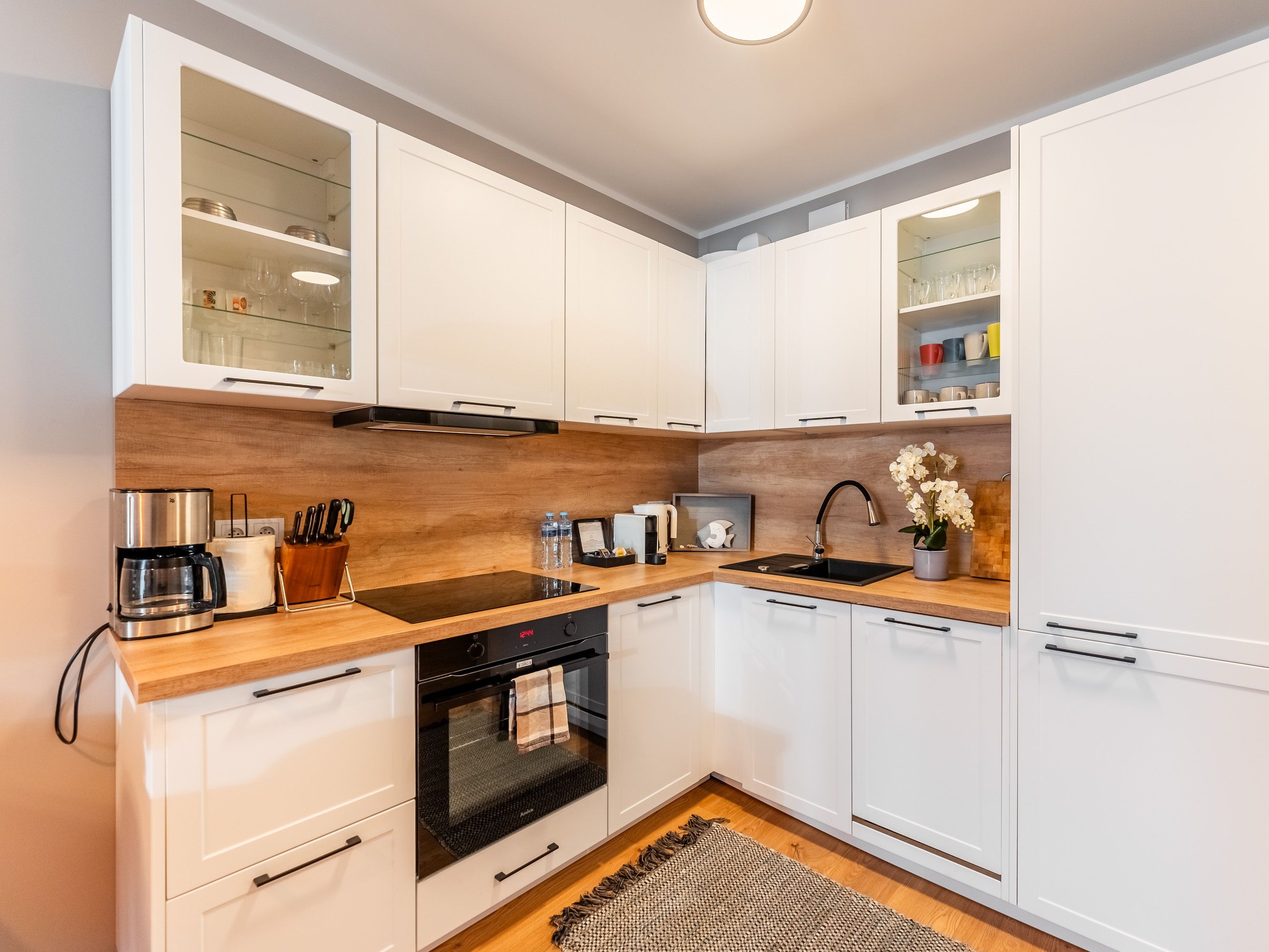 Una cocina moderna con armarios blancos, encimera de madera, horno integrado y un fregadero.