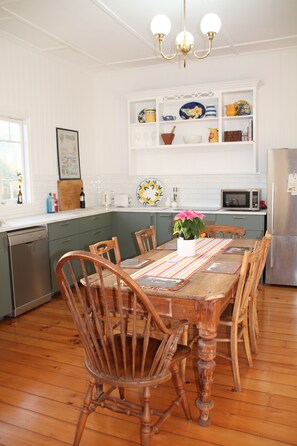 A kitchen with wooden cabinets, a dining table with chairs, a refrigerator, and a microwave. - Charming cottage in the heart of Maleny. Two minute walk from the main street. (Maleny)