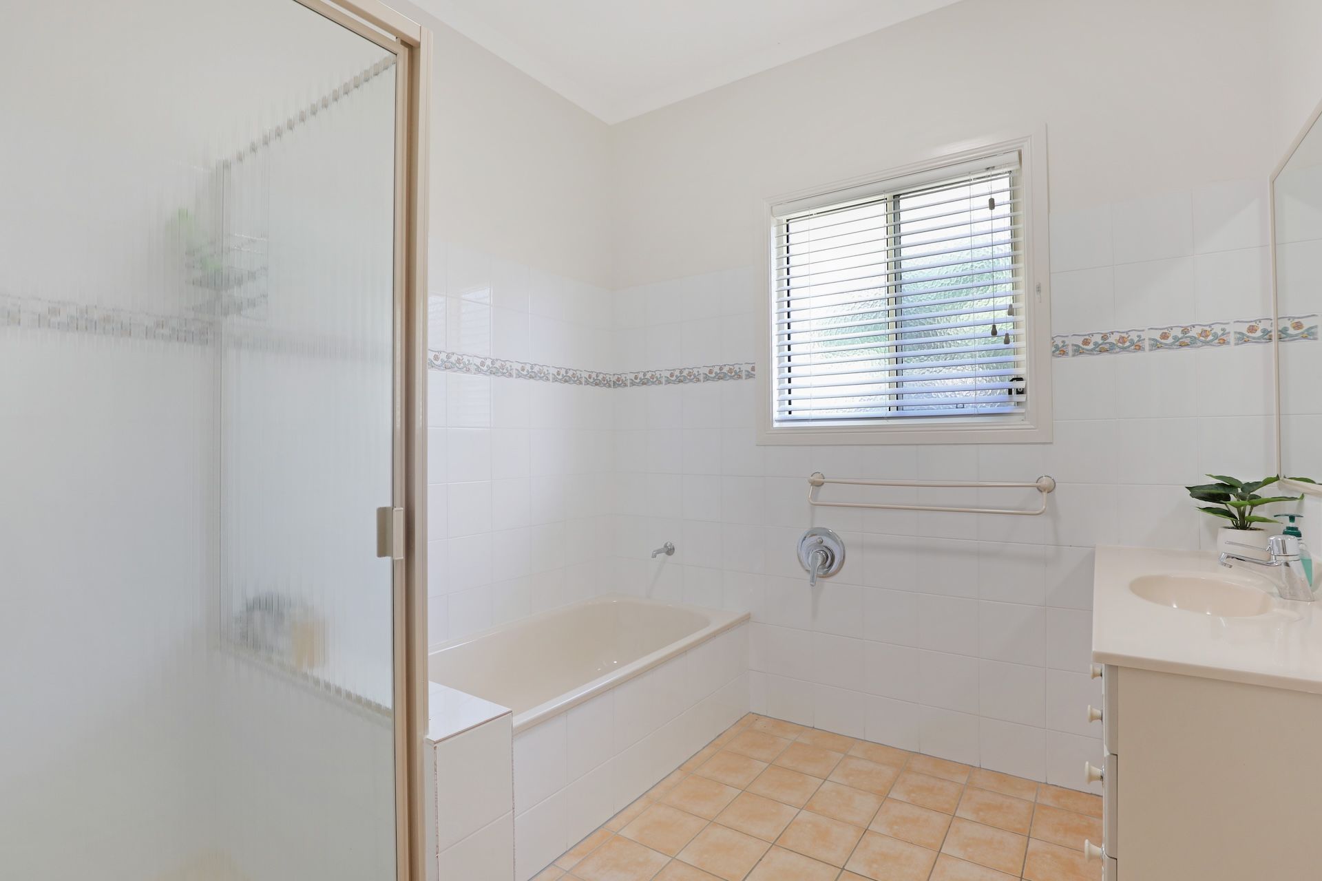 A bathroom with a bathtub, a window with blinds, a towel rack, and a sink with a mirror.