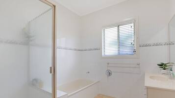 A bathroom with a bathtub, a window with blinds, a towel rack, and a sink with a mirror.