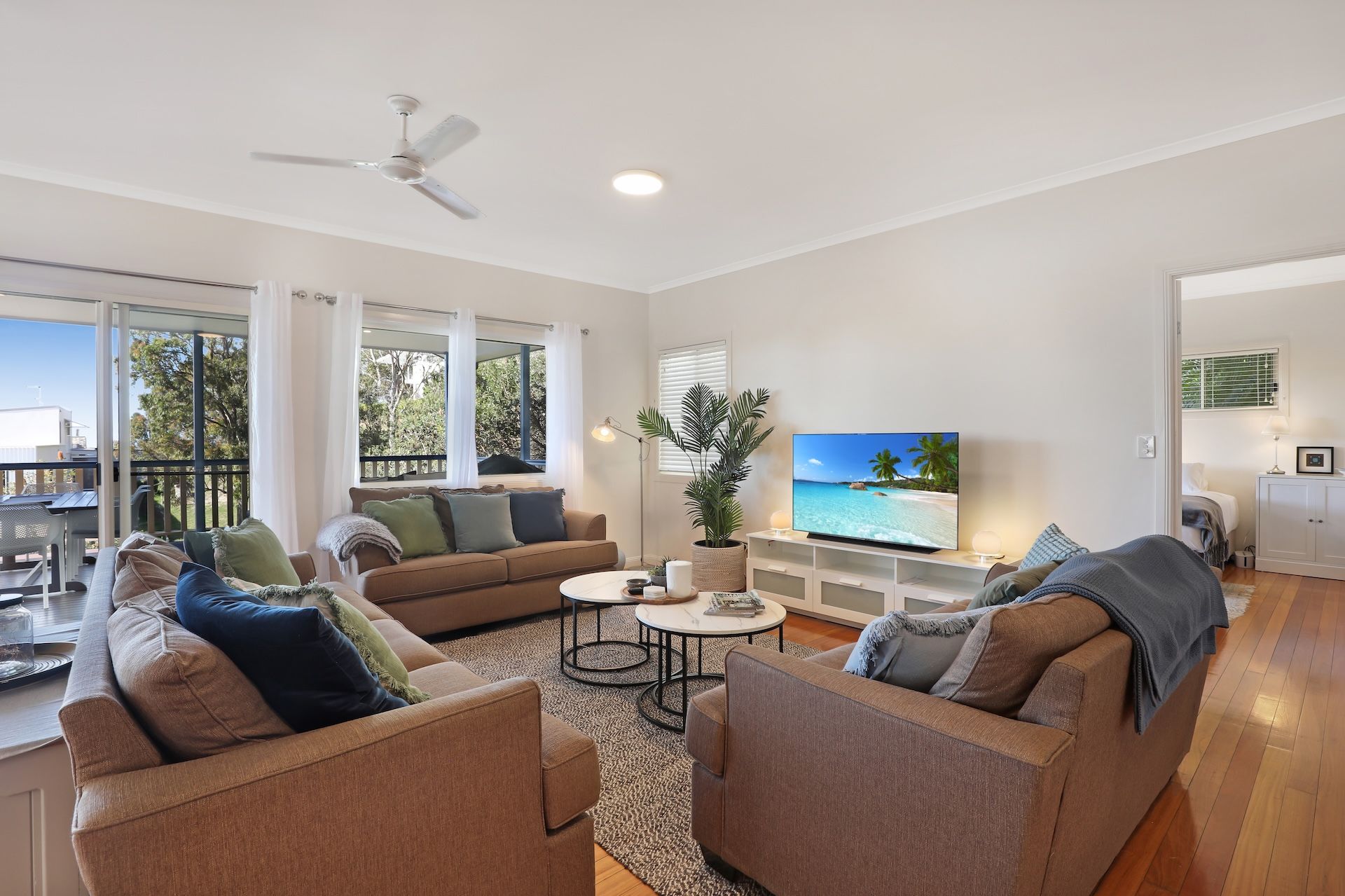 A spacious living room with a large television, comfortable seating, and a balcony with a view.