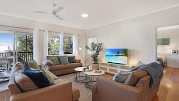 A spacious living room with a large television, comfortable seating, and a balcony with a view.