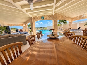 A spacious outdoor dining area with a pool view, stone pillars, and a ceiling fan. - New 5-bedroom family villa in Esmeralda-noord, just 3 minutes from Arashi Beach. Enjoy peaceful Salinja views, a beautiful private pool, natural stone details, a covered outdoor patio with BBQ, 5 king bedrooms, a full kitchen,and space for 10 Guests (Noord)