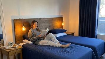 Une chambre avec deux lits, une table de chevet, une lampe et une fenêtre avec des rideaux.