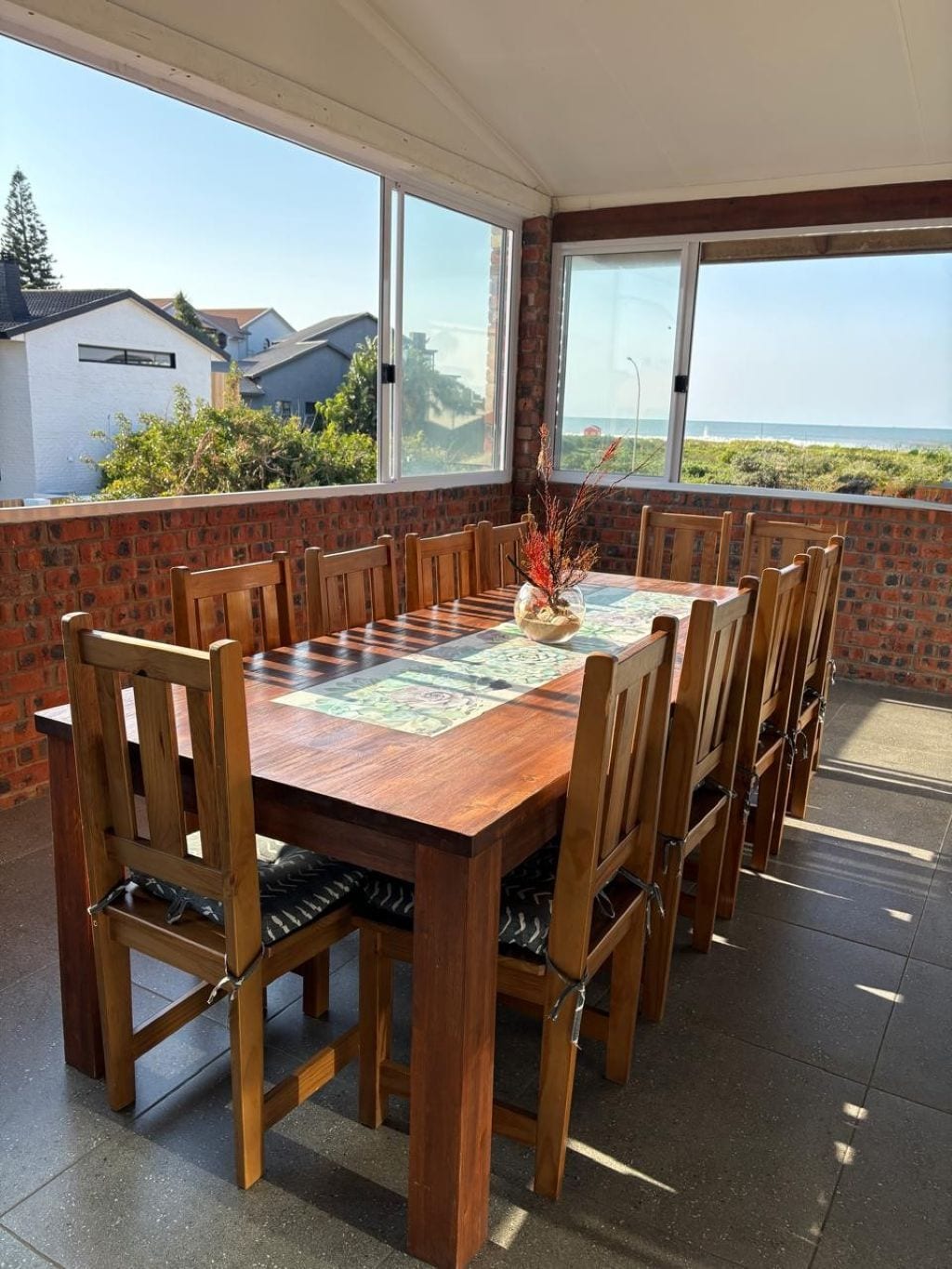 Un espace extérieur aménagé pour les repas, avec une table et des chaises en bois, un vase décoratif et une vue sur la mer.