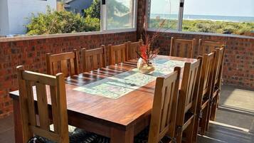 Un espace extérieur aménagé pour les repas, avec une table et des chaises en bois, un vase décoratif et une vue sur la mer.