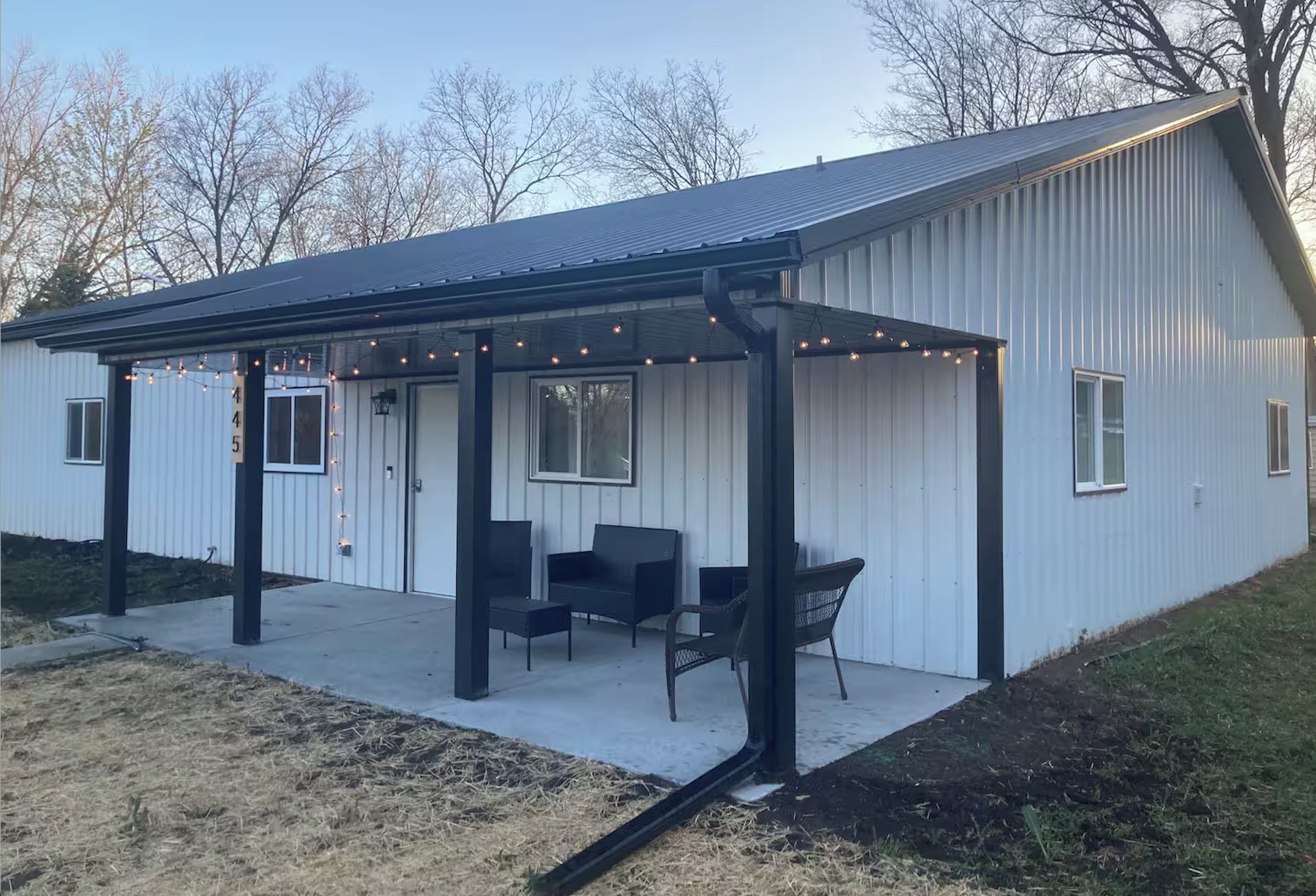 A metal building with a covered patio area, two chairs, and a string of lights.