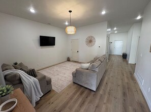 Una sala de estar moderna con un televisor de pantalla plana, un sofá gris, un tapete estampado y piso de madera.