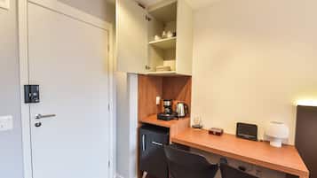 Una kitchenette compacta con horno integrado, cafetera y un pequeño armario sobre la encimera.