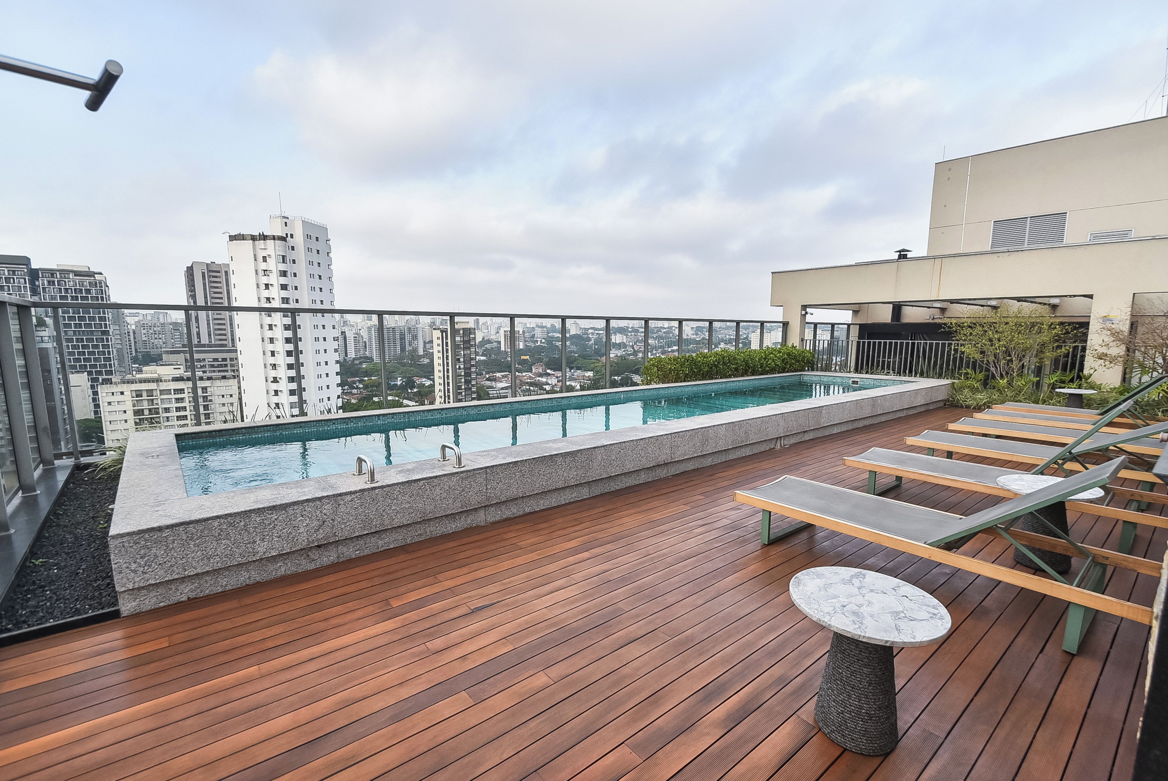 A rooftop pool area with a wooden deck, lounge chairs, and a view of the cityscape.