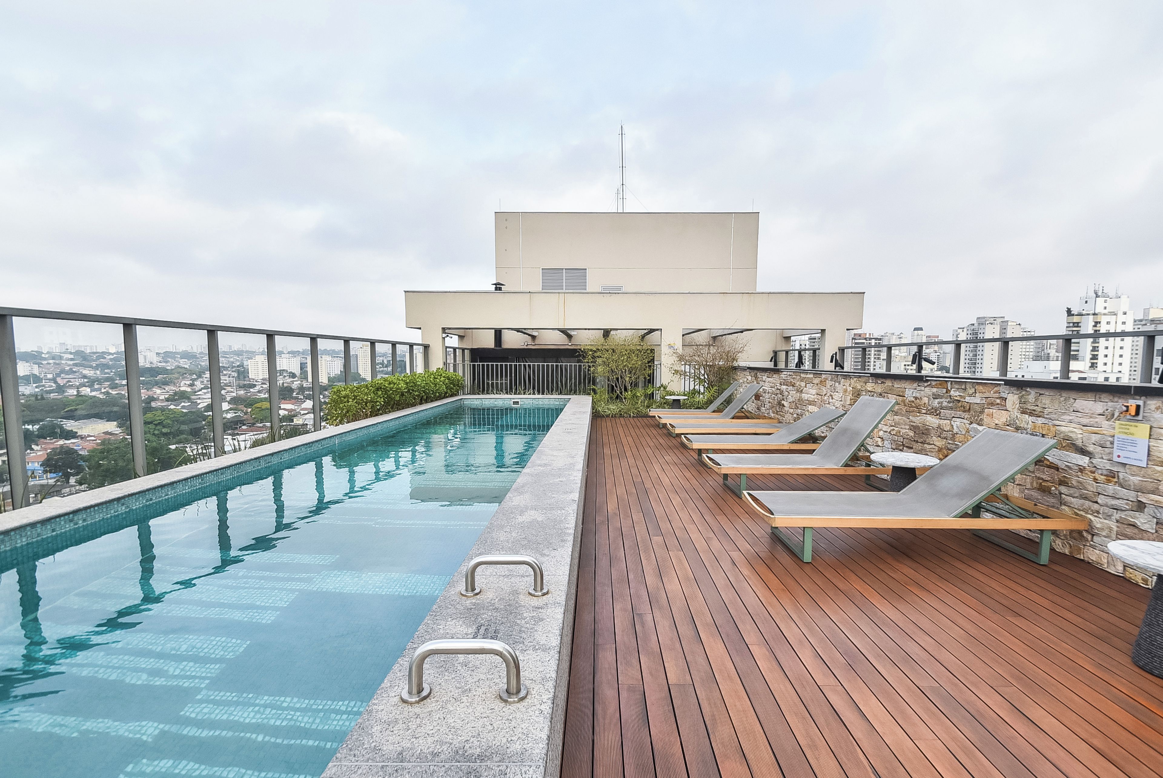 A rooftop pool with a view of the city, wooden deck, and lounge chairs.