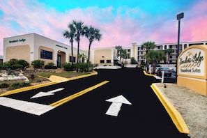A hotel entrance with a sign for 'Bendini's Lodge Oceanfront Suites', a parking lot with directional arrows, and palm trees. - Beacher's Oceanfront Balcony, Condo Complex Construction 10/2026-1/2027 (St. Augustine)