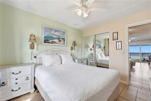 A bedroom with a bed, bedside tables, a nightstand, a ceiling fan, a painting, and a balcony door. - Beacher's Oceanfront Balcony, Condo Complex Construction 10/2026-1/2027 (St. Augustine)
