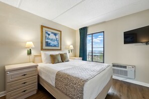 Ein Hotelzimmer mit Bett, Nachttischen, Fernseher, Fenster mit Aussicht und Klimaanlage.