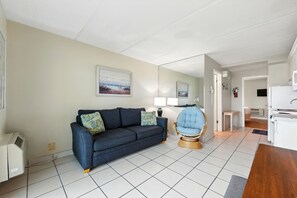 Ein Wohnzimmer mit einer Couch, einem Sessel, einer Lampe und einem Bild an der Wand.