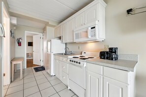 A kitchen with white cabinets, a microwave, a stove, and a coffee maker. - Beacher's Oceanfront Balcony, Condo Complex Construction 10/2026-1/2027 (St. Augustine)