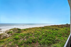 Eine Küstenlandschaft mit Strand, grasbewachsenen Dünen und einem hölzernen Steg, der zum Wasser führt.
