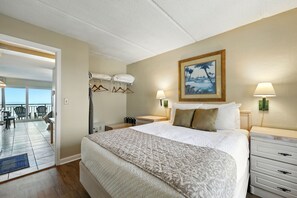 Ein Hotelzimmer mit Bett, Schreibtisch, Stuhl, einem Balkon mit Sitzgelegenheiten und einem Bild an der Wand.