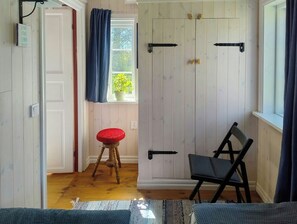A room with a wooden door, a window with a view of greenery, a red stool, and a black chair. - Cozy stone cottage on Gotlaand (Burgsvik)