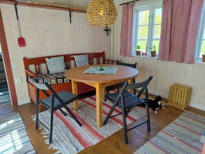 Ein gemütlicher Essbereich mit einem Holztisch, schwarzen Stühlen, einer gewebten Leuchte und einem Fenster mit gestreiften Vorhängen.