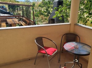 A balcony with two chairs and a small table, overlooking a garden and a barbecue area. - Apartments Marija Sukosan - Classic One Bedroom Apartment (Sukosan)