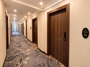 Pasillo de hotel con alfombra estampada, puertas de madera y un letrero que indica la habitación 306.