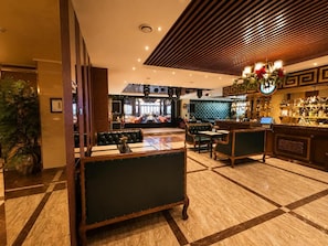 Un hall de hotel con zona de bar, arreglos de asientos y un mostrador de recepción.