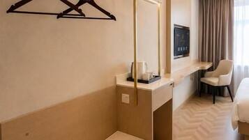 A hotel room with a bed, a desk, a chair, a TV, and a wardrobe with hangers.