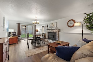 A living room with a fireplace, a dining area with a chandelier, and a sofa with cushions. - Your CDA Escape | Minutes to Downtown (Coeur D Alene)