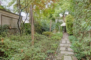 Ein steiniger Weg schlängelt sich durch einen üppigen Garten mit dichtem Grün und einem Bambuszaun.