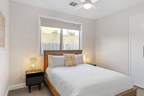Ein Schlafzimmer mit einem Bett, zwei Nachttischlampen, einem Deckenventilator und einem Fenster mit Blick auf eine Ziegelmauer.
