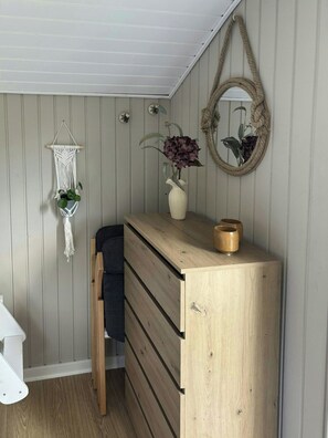 A compact room with a wooden dresser, a macrame wall hanging, a mirror, and a vase with flowers. - Holiday home with hot tub and orchard in Pøt (Hedensted)
