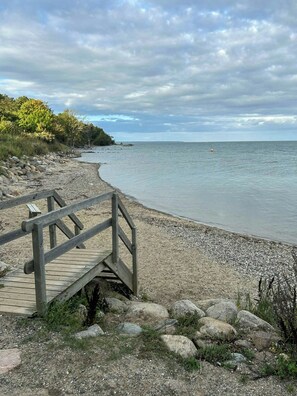 Ein hölzerner Steg führt zu einem Kiesstrand mit Blick auf das Meer und das entfernte Land.