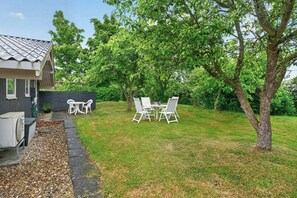 Ein Wohnhausgarten mit Terrassentisch und -stühlen, einem kleinen Geräteschuppen und einem großen Baum.
