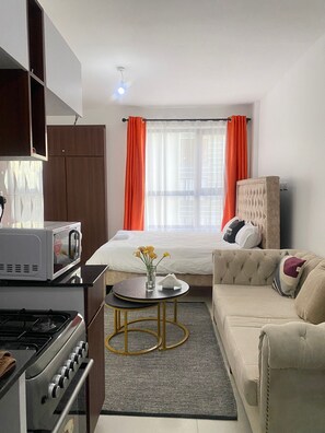 Habitación de hotel pequeña con cama, sofá, mesita con un florero, microondas y estufa.
