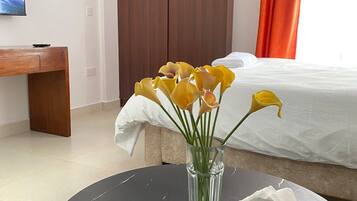 Quarto de hotel com uma cama, um guarda-roupa de madeira, uma mesa redonda com um vaso de flores e uma televisão na parede.