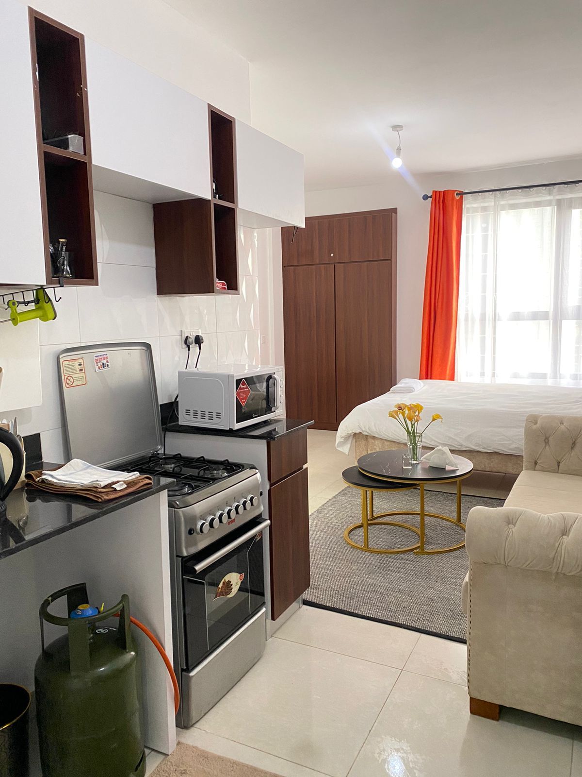 A compact kitchen with a gas stove, oven, microwave, and a small refrigerator. There is a dining area with a round table and a sofa.