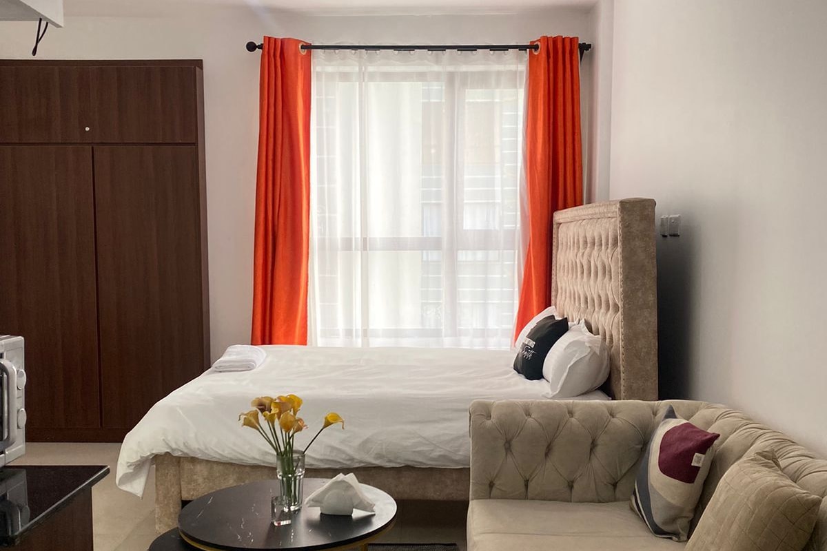 Quarto de hotel com cama, sofá, mesa redonda pequena com um vaso de flores e guarda-roupa.