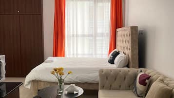 Quarto de hotel com cama, sofá, mesa redonda pequena com um vaso de flores e guarda-roupa.